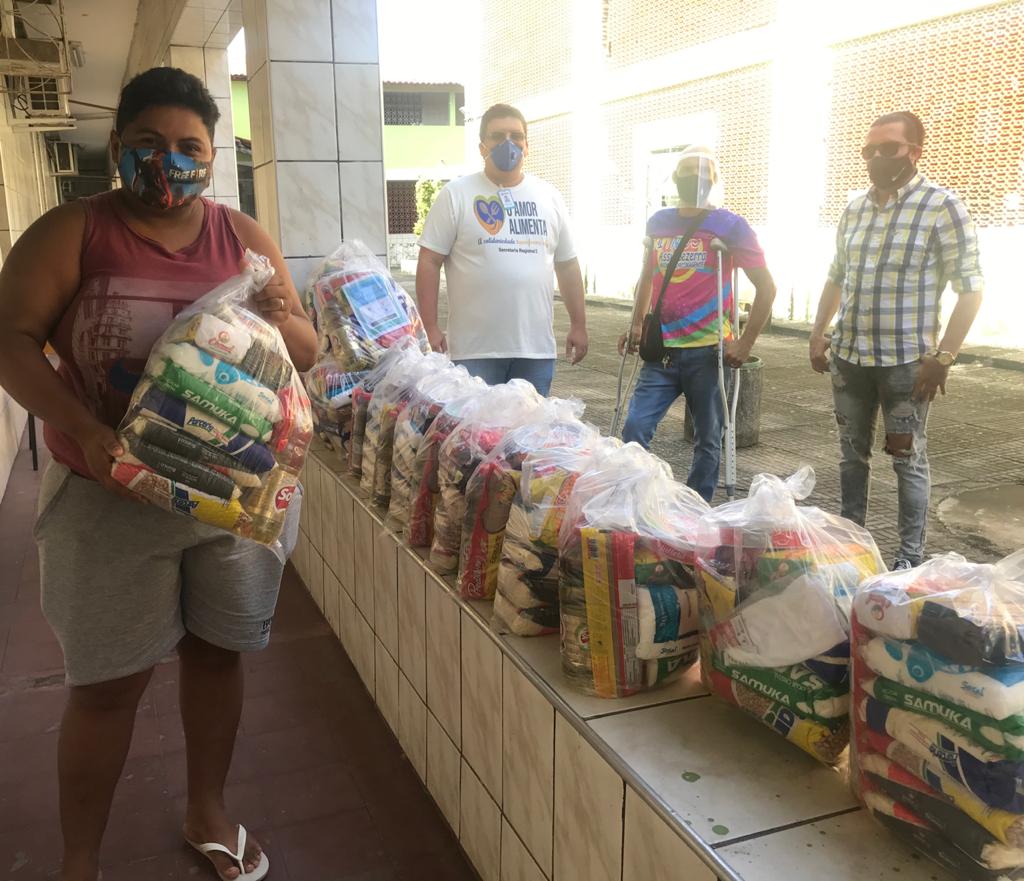 dois homens e duas mulheres usando máscaras e protetores de rosto posando para a foto ao lado de várias cestas básicas empilhadas